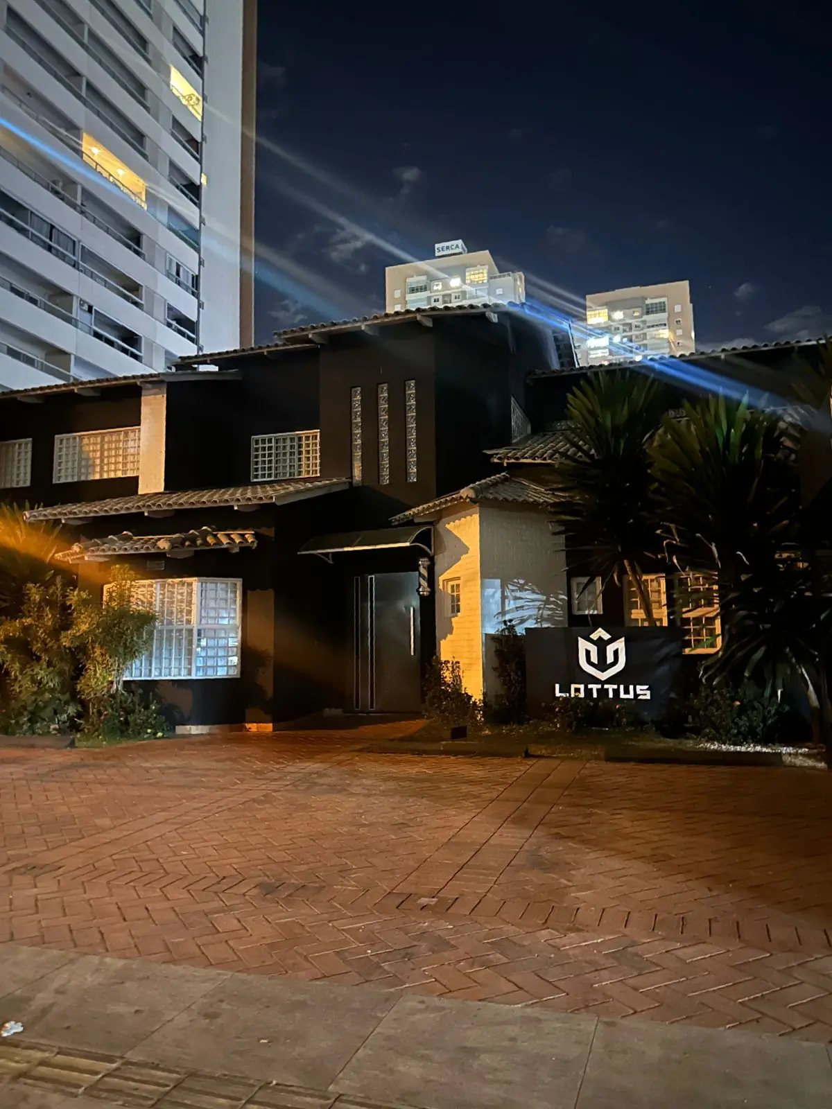 Fachada da Lottus Barbearia Clube à noite, no Jardim América, com o letreiro iluminado