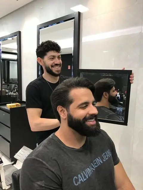 Junior Araujo mostrando o resultado do corte ao cliente no espelho